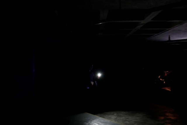 A woman uses light from a phone to find her car at a parking garage during a blackout in Caracas, Venezuela February 6, 2018. REUTERS/Carlos Garcia Rawlins